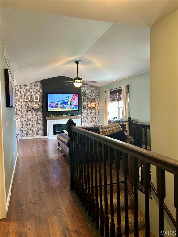 corridor with wood finished floors, vaulted ceiling, an upstairs landing, baseboards, and wallpapered walls