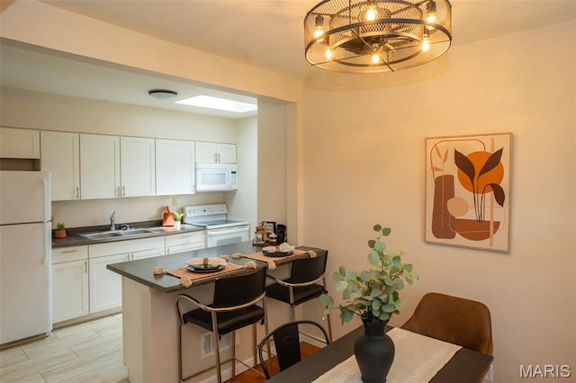 2917 Grand Ave, Granite City, IL 62040 - kitchen with white appliances, white cabinets, a kitchen bar, a chandelier, and dark countertops