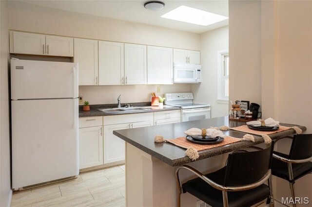 2917 Grand Ave, Granite City, IL 62040 - kitchen featuring white appliances, a skylight, dark countertops, white cabinetry, and a kitchen breakfast bar