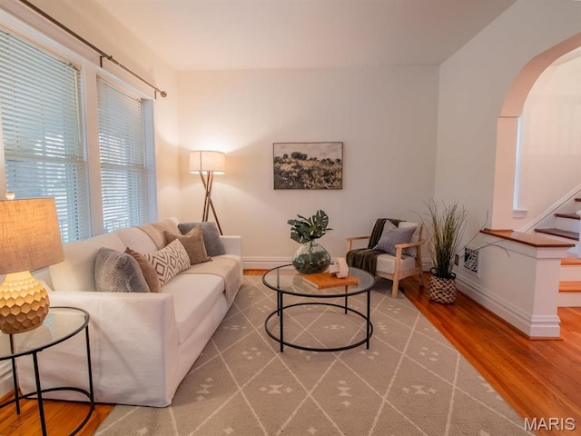 living area with wood finished floors, arched walkways, stairway, and baseboards