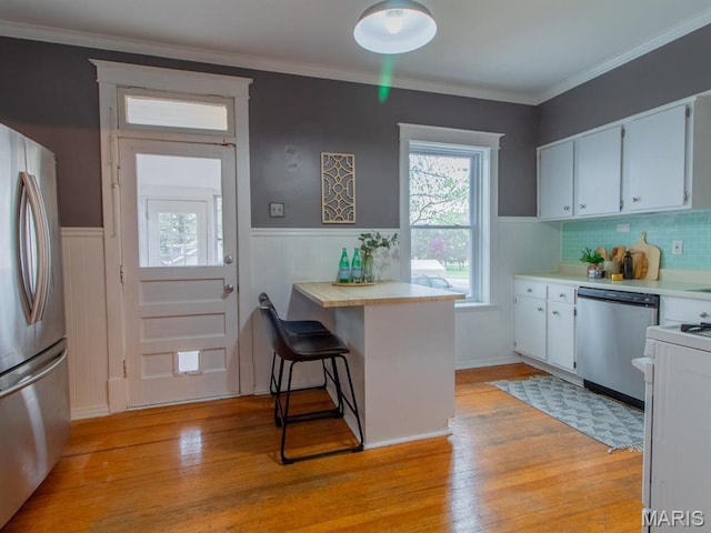 kitchen with appliances with stainless steel finishes, light countertops, wainscoting, light wood finished floors, and plenty of natural light