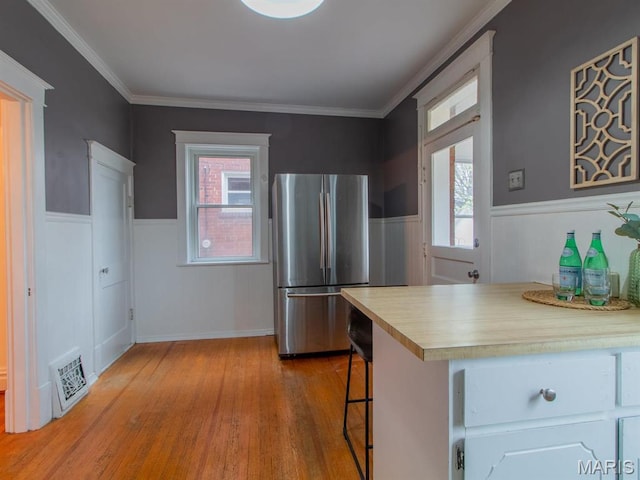 kitchen featuring freestanding refrigerator, wood finished floors, a wainscoted wall, healthy amount of natural light, and crown molding