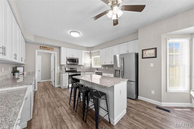 11 Country Crossing Estates Dr, Saint Peters, MO 63376 - kitchen with appliances with stainless steel finishes, a kitchen bar, wood finished floors, white cabinetry, and a textured ceiling