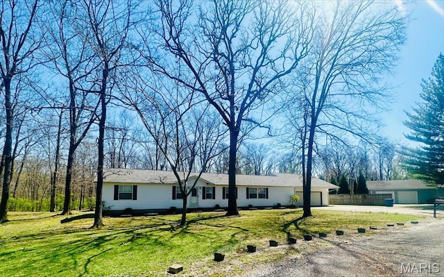 ranch-style home featuring dirt driveway, an attached garage, and a front lawn