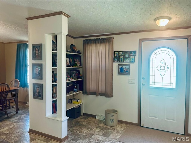 foyer featuring a textured ceiling, stone finish floors, baseboards, and ornamental molding