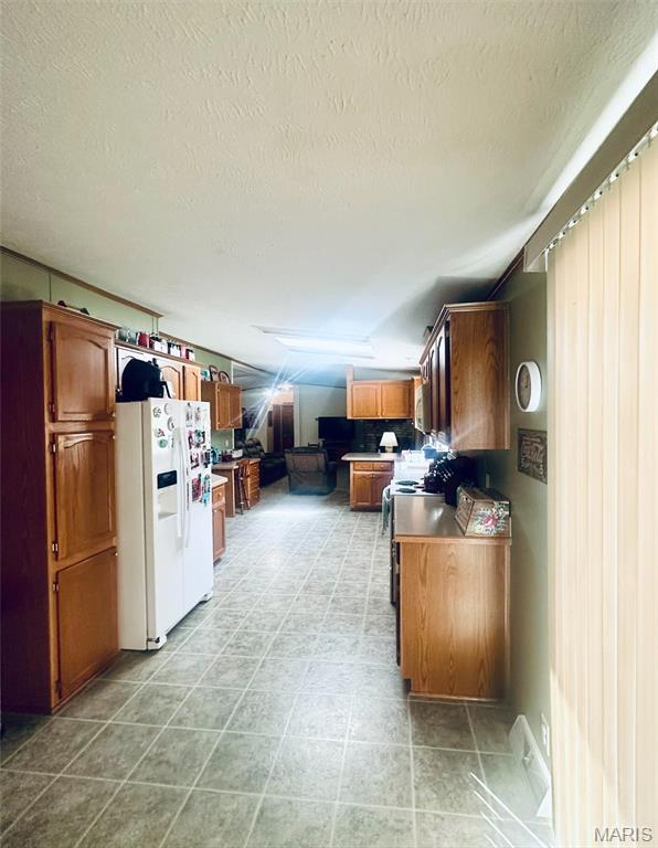 kitchen featuring white refrigerator with ice dispenser, a textured ceiling, brown cabinets, and electric stove