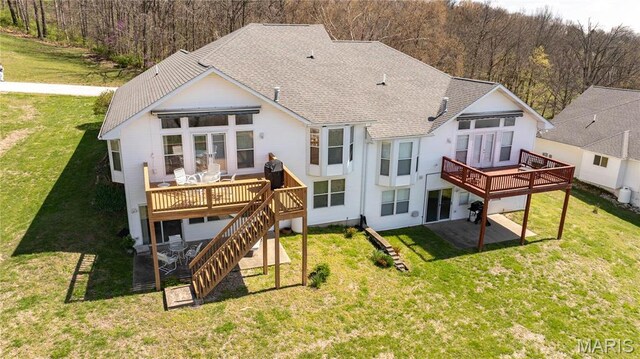 back of property with a wooden deck, roof with shingles, a yard, and a view of trees