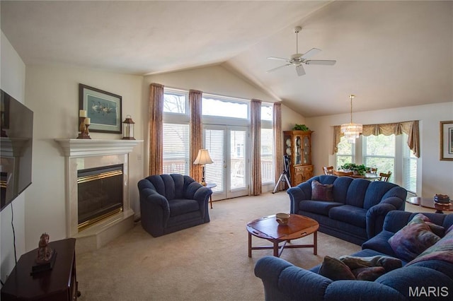 living room featuring light carpet, vaulted ceiling, a tiled fireplace, ceiling fan, and a chandelier