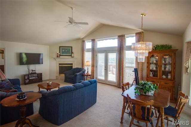 living room featuring light colored carpet, vaulted ceiling, a ceiling fan, a fireplace with raised hearth, and a chandelier