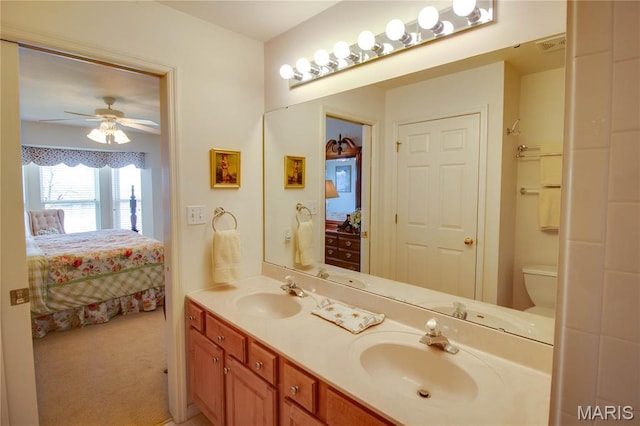 ensuite bathroom with double vanity, a ceiling fan, and toilet