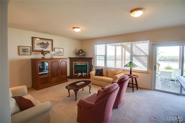 living room with light colored carpet, healthy amount of natural light, a fireplace with raised hearth, and a water view