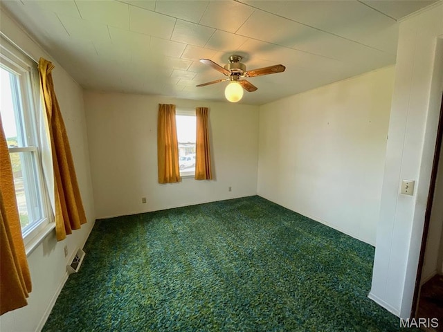 spare room with plenty of natural light, dark colored carpet, and ceiling fan