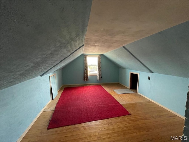 bonus room featuring wood finished floors, baseboards, lofted ceiling, and a textured ceiling
