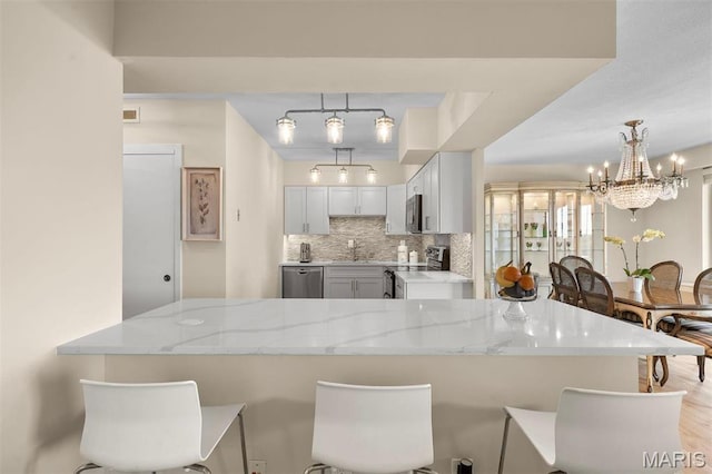 kitchen featuring appliances with stainless steel finishes, a breakfast bar area, decorative backsplash, light stone counters, and hanging light fixtures