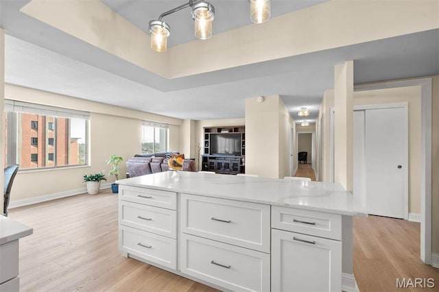 kitchen with open floor plan, white cabinets, light wood finished floors, baseboards, and a kitchen island