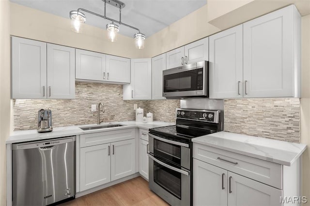 kitchen with appliances with stainless steel finishes, a sink, light wood finished floors, backsplash, and light stone countertops