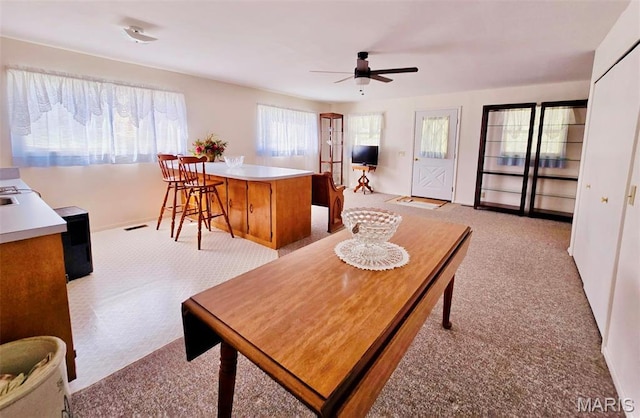 living area featuring light carpet, ceiling fan, and baseboards