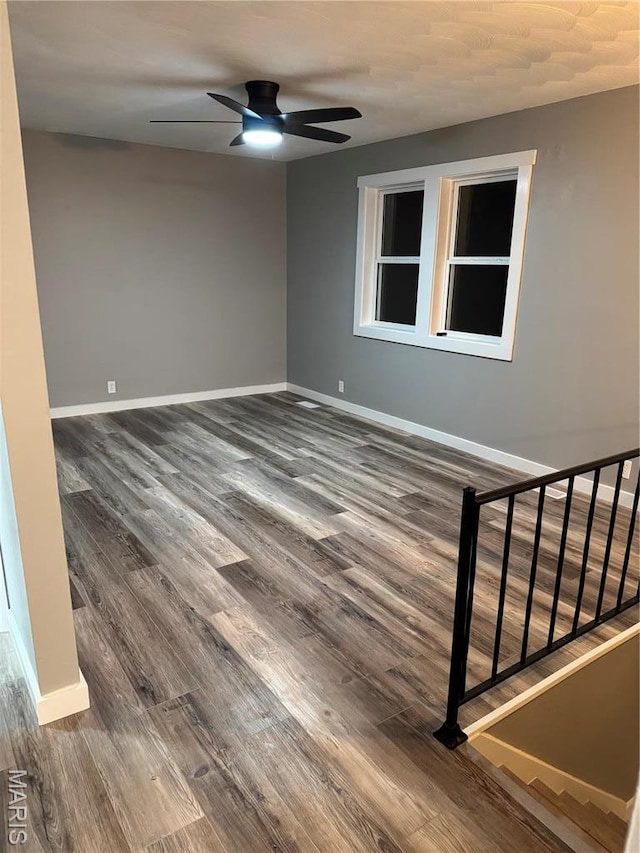 unfurnished room featuring ceiling fan, dark wood-style floors, baseboards, and stairs