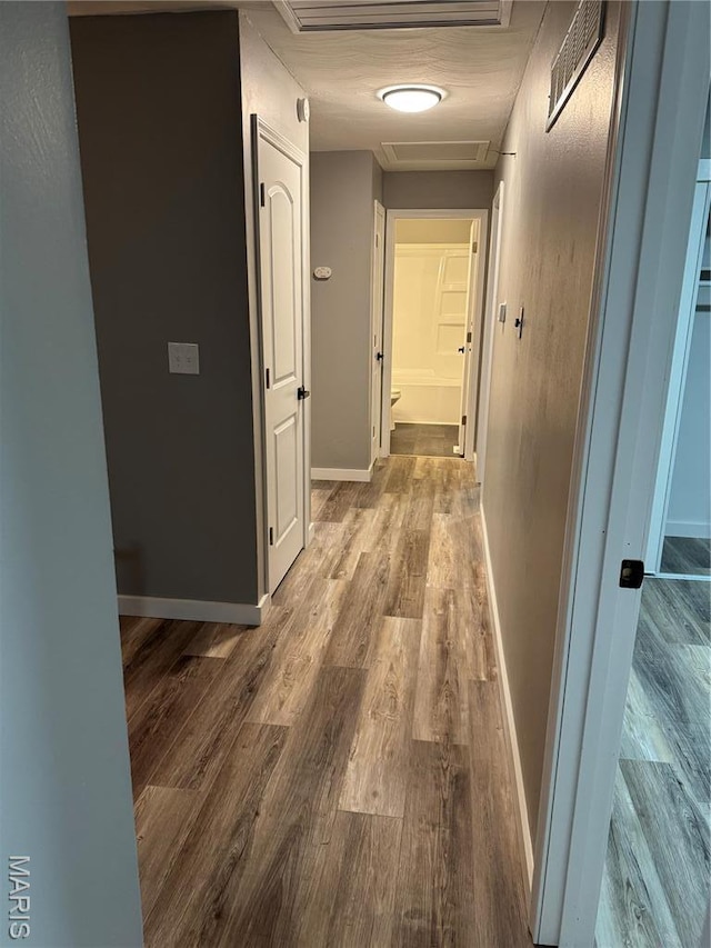 corridor with wood finished floors, baseboards, and attic access