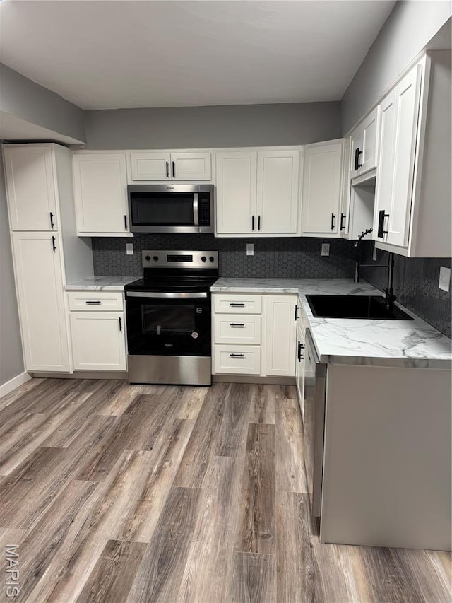 kitchen featuring appliances with stainless steel finishes, a sink, decorative backsplash, wood finished floors, and white cabinets