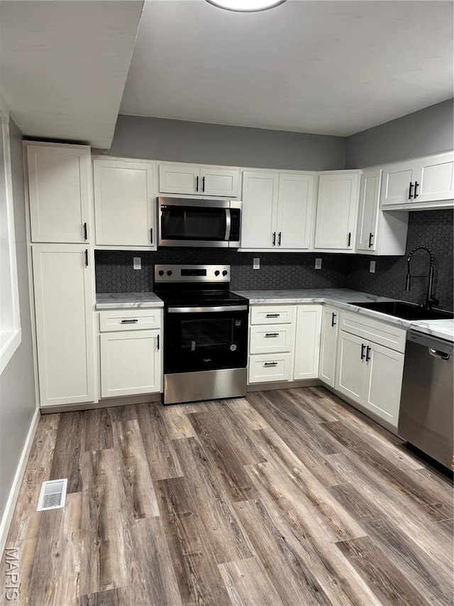 kitchen featuring appliances with stainless steel finishes, a sink, white cabinets, and tasteful backsplash