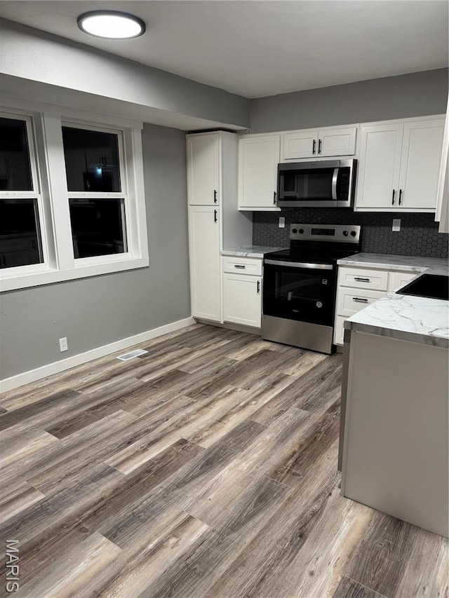 kitchen featuring appliances with stainless steel finishes, white cabinets, wood finished floors, a sink, and light stone counters