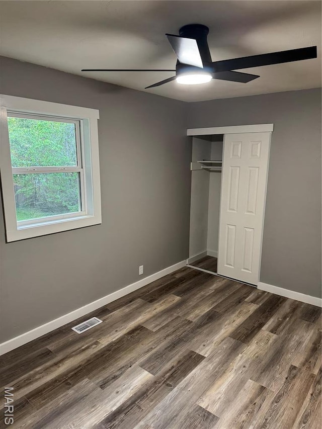 unfurnished bedroom featuring dark wood finished floors, a closet, baseboards, and a ceiling fan