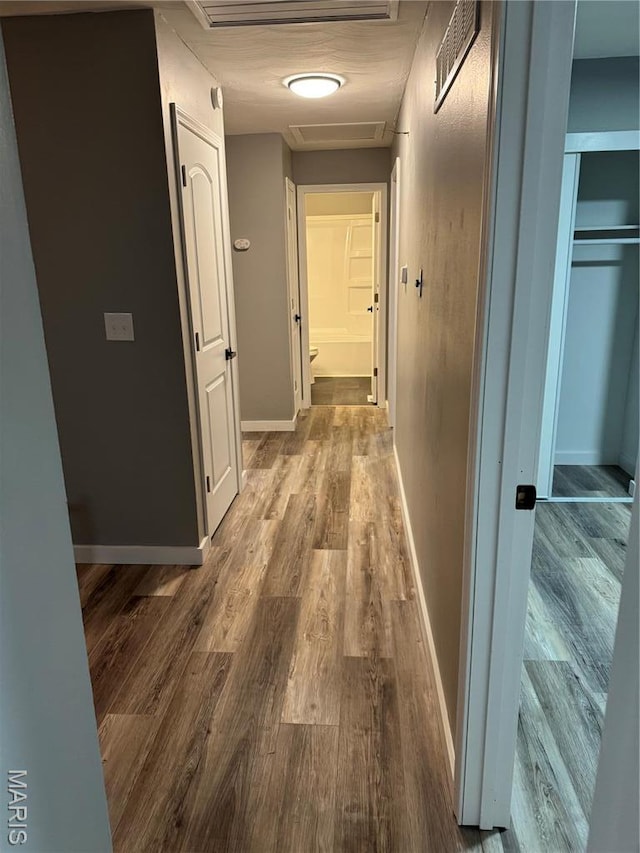 hallway featuring wood finished floors, attic access, and baseboards