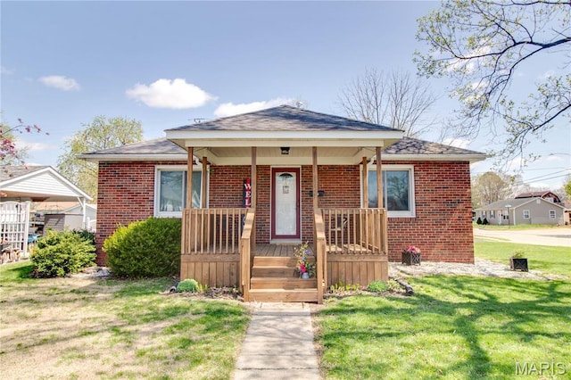 bungalow featuring brick siding, covered porch, a front lawn, and roof with shingles