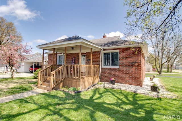 view of front of house with brick siding, a front yard, a chimney, a shingled roof, and a porch