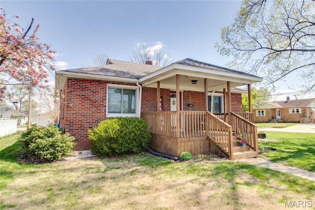 view of front of home featuring brick siding, a front yard, a porch, and a shingled roof