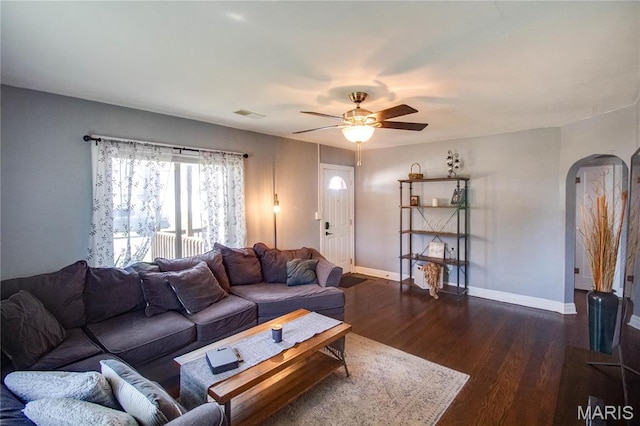 living room featuring arched walkways, dark wood-style flooring, baseboards, and ceiling fan