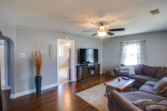 living area featuring arched walkways, ceiling fan, dark wood-style flooring, and baseboards