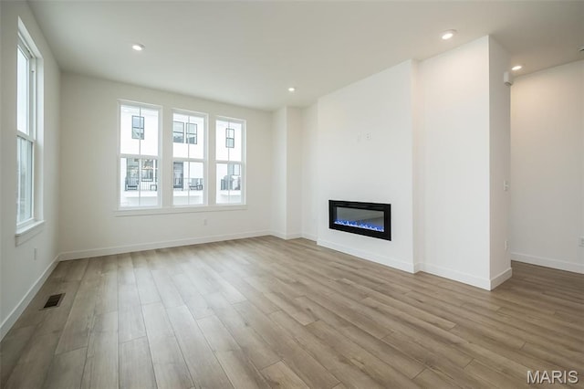 unfurnished living room with wood finished floors, a glass covered fireplace, baseboards, and recessed lighting