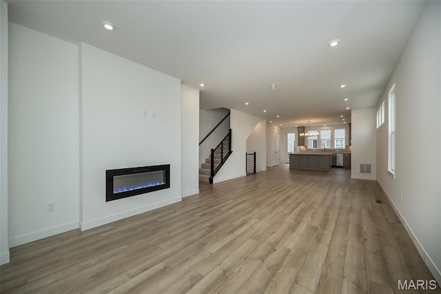 unfurnished living room featuring light wood-type flooring, stairway, a glass covered fireplace, recessed lighting, and baseboards
