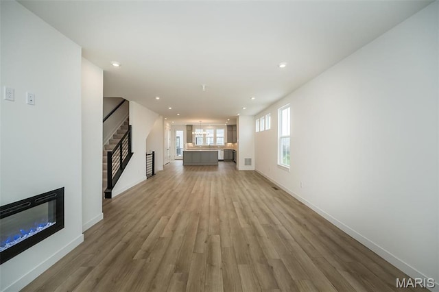 unfurnished living room featuring a glass covered fireplace, light wood-type flooring, recessed lighting, and baseboards