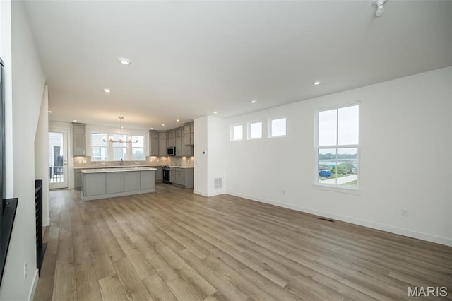 unfurnished living room with light wood-style floors, recessed lighting, baseboards, and a chandelier