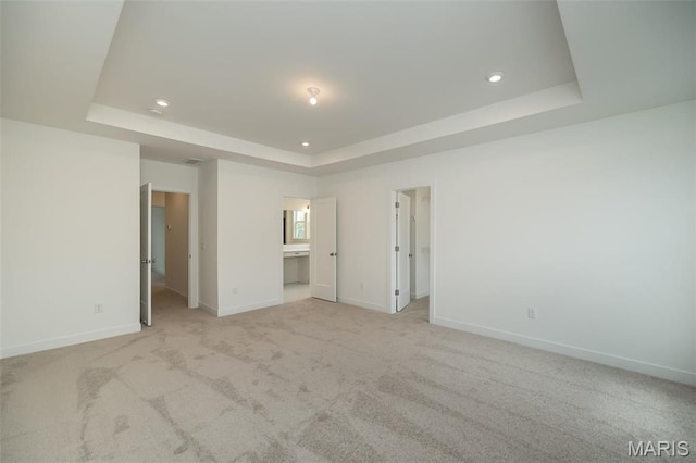 unfurnished bedroom featuring a walk in closet, a tray ceiling, recessed lighting, baseboards, and light colored carpet