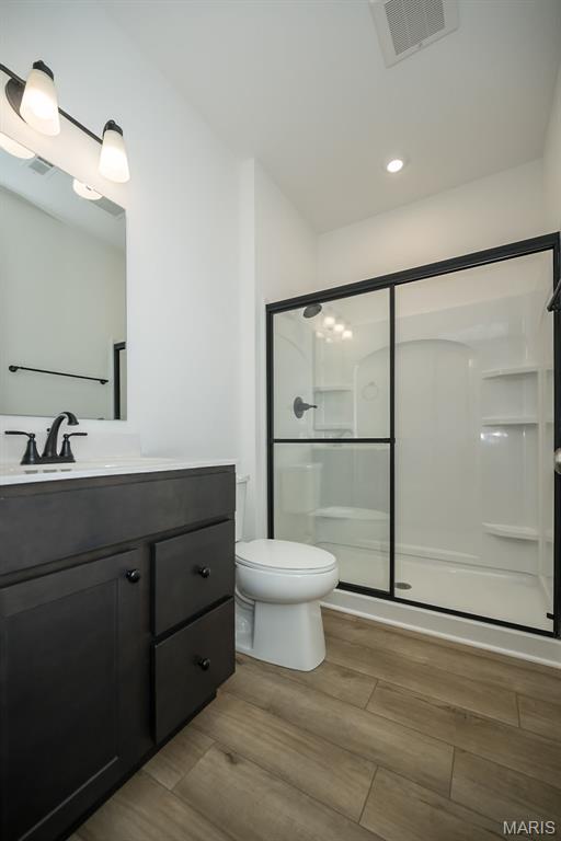 full bath with a shower stall, vanity, toilet, wood finished floors, and recessed lighting
