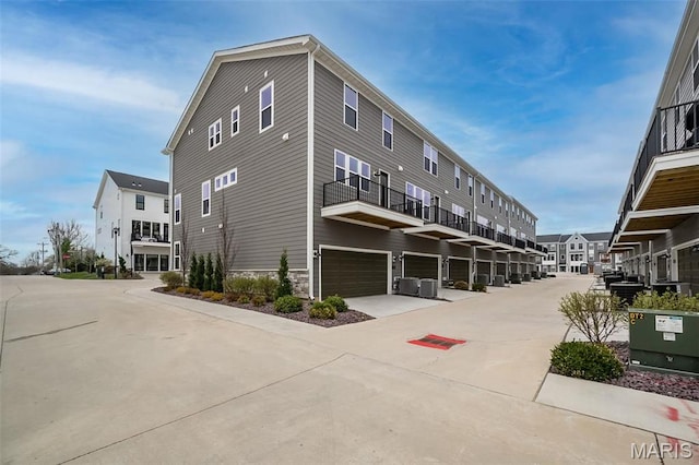 view of side of property featuring an attached garage, stone siding, concrete driveway, a balcony, and cooling unit