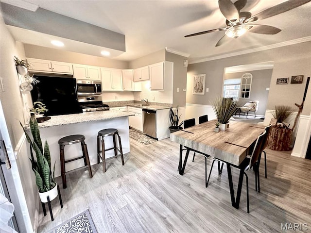 kitchen featuring appliances with stainless steel finishes, a sink, a peninsula, white cabinets, and ornamental molding