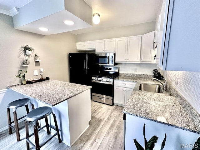 kitchen with appliances with stainless steel finishes, a sink, decorative backsplash, light wood-type flooring, and a breakfast bar area