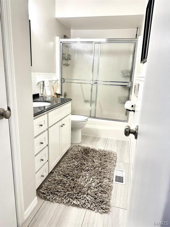 full bath featuring vanity, wood finished floors, toilet, and combined bath / shower with glass door
