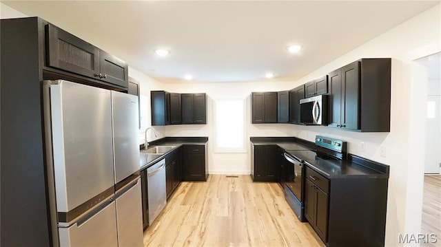 kitchen featuring stainless steel appliances, a sink, dark countertops, light wood-type flooring, and recessed lighting