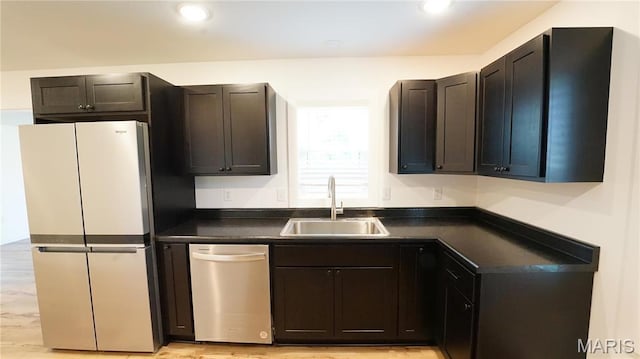 kitchen with appliances with stainless steel finishes, a sink, dark countertops, light wood-style floors, and recessed lighting