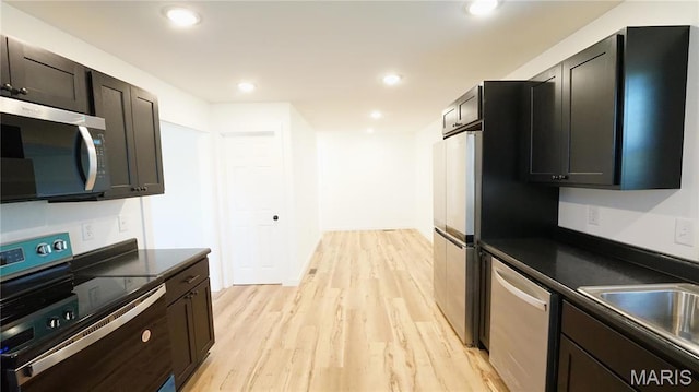 kitchen featuring appliances with stainless steel finishes, dark countertops, light wood-style floors, a sink, and recessed lighting