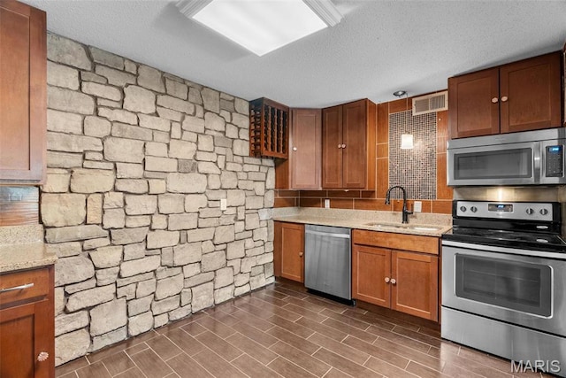 2793 Blackforest Dr Unit B, Saint Louis, MO 63129 - kitchen featuring stainless steel appliances, a sink, a textured ceiling, brown cabinetry, and light stone countertops