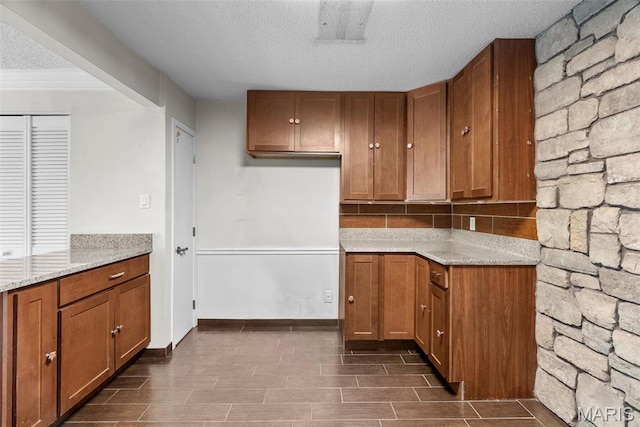 2793 Blackforest Dr Unit B, Saint Louis, MO 63129 - kitchen featuring brown cabinetry, a textured ceiling, light stone countertops, dark wood-type flooring, and baseboards