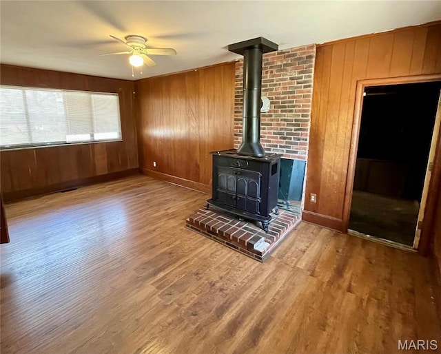 11606 Herefordshire Dr, Saint Louis, MO 63138 - unfurnished living room featuring a wood stove, wooden walls, wood finished floors, a ceiling fan, and baseboards