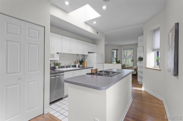 5858 Nina Pl Unit 3E, Saint Louis, MO 63112 - kitchen featuring stainless steel appliances, white cabinetry, a sink, a kitchen island, and light wood-style flooring